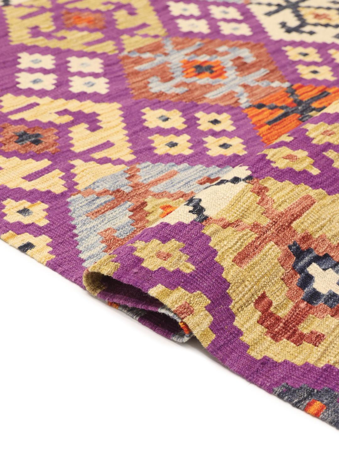 Et håndvævet Kelim-tæppe fra Afghanistan med en lilla bund og geometriske motiver.