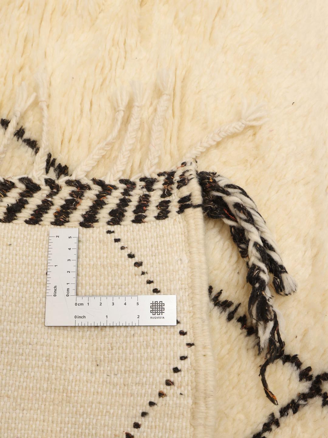 Et rektangulært håndlavet marokkansk berbertæppe med en beige baggrund og et sort diamantmønster.