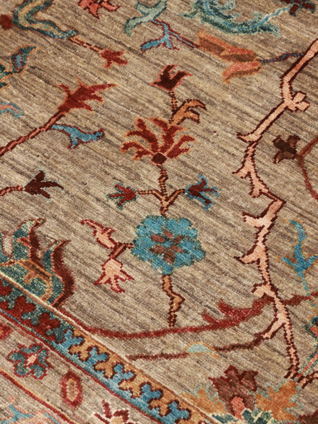 Et håndknyttet afghansk tæppe med blomstermotiver i beige, blå og røde toner.