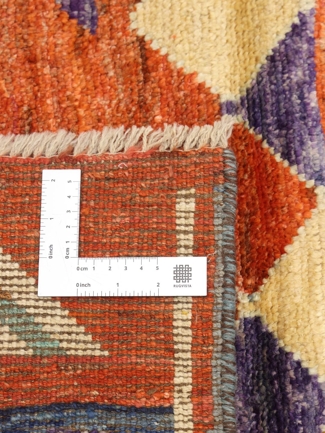 Håndknyttet afghansk tæppe med en orange flade og farverige geometriske mønstre.