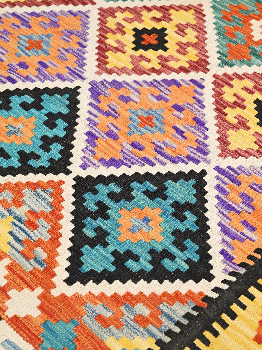 A hand-woven, one-of-a-kind Kelim rug from Afghanistan featuring a multicoloured geometric diamond pattern.