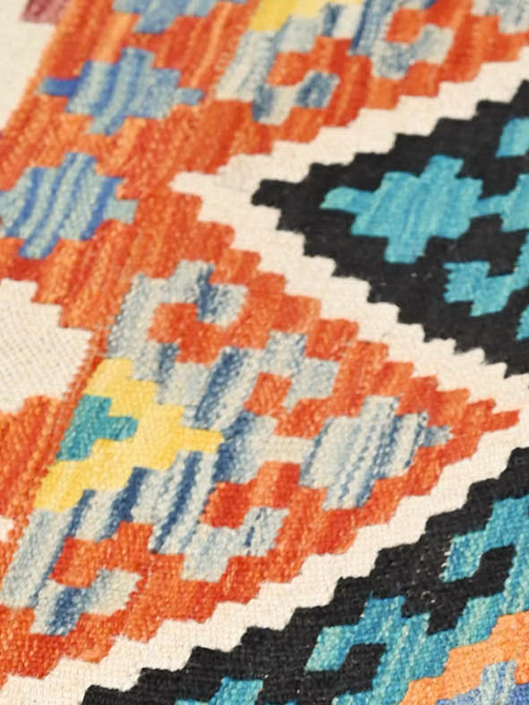 A hand-woven, one-of-a-kind Kelim rug from Afghanistan featuring a multicoloured geometric diamond pattern.