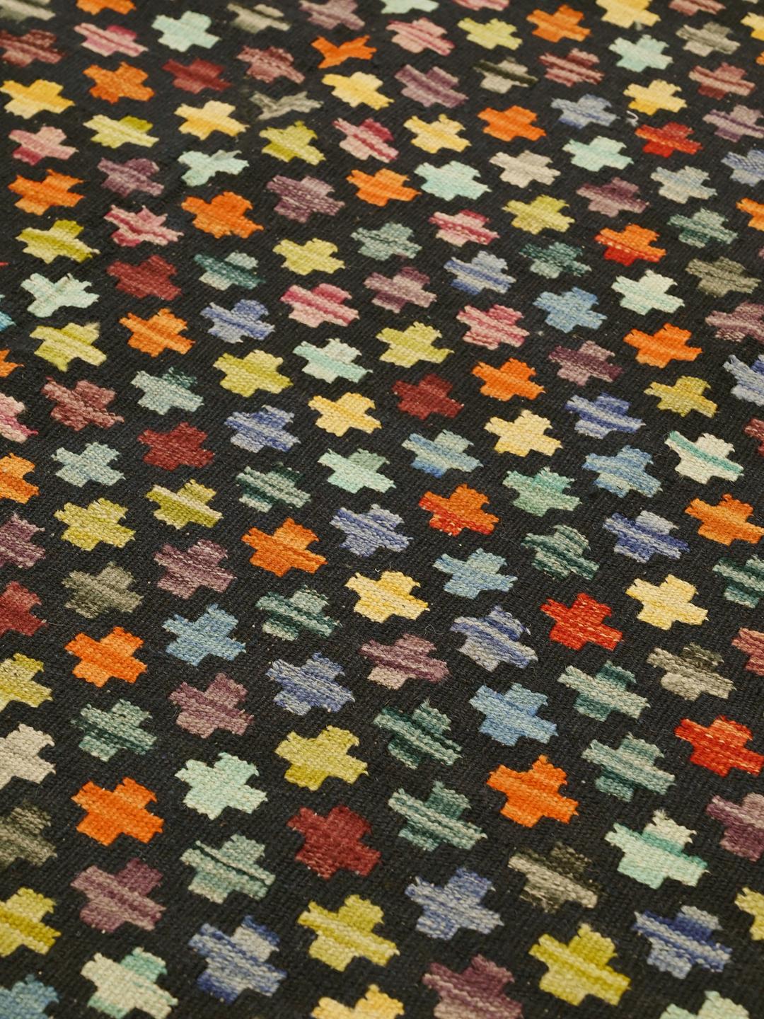 Et håndvævet afghansk Kelim-tæppe med en sort bund og farverige geometriske motiver