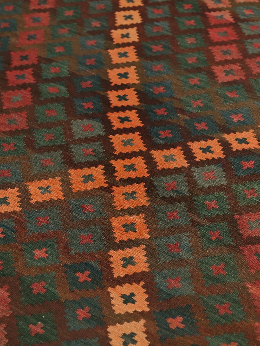 Et håndvævet Maimane-kelimtæppe fra Afghanistan med geometriske mønstre i mørkebrun og rød.