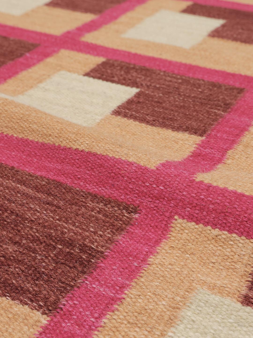 Roze en meerkleurig tapijt met een geometrisch patroon op een houten vloer.