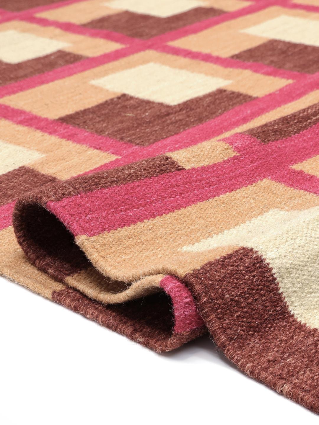 Roze en meerkleurig tapijt met een geometrisch patroon op een houten vloer.