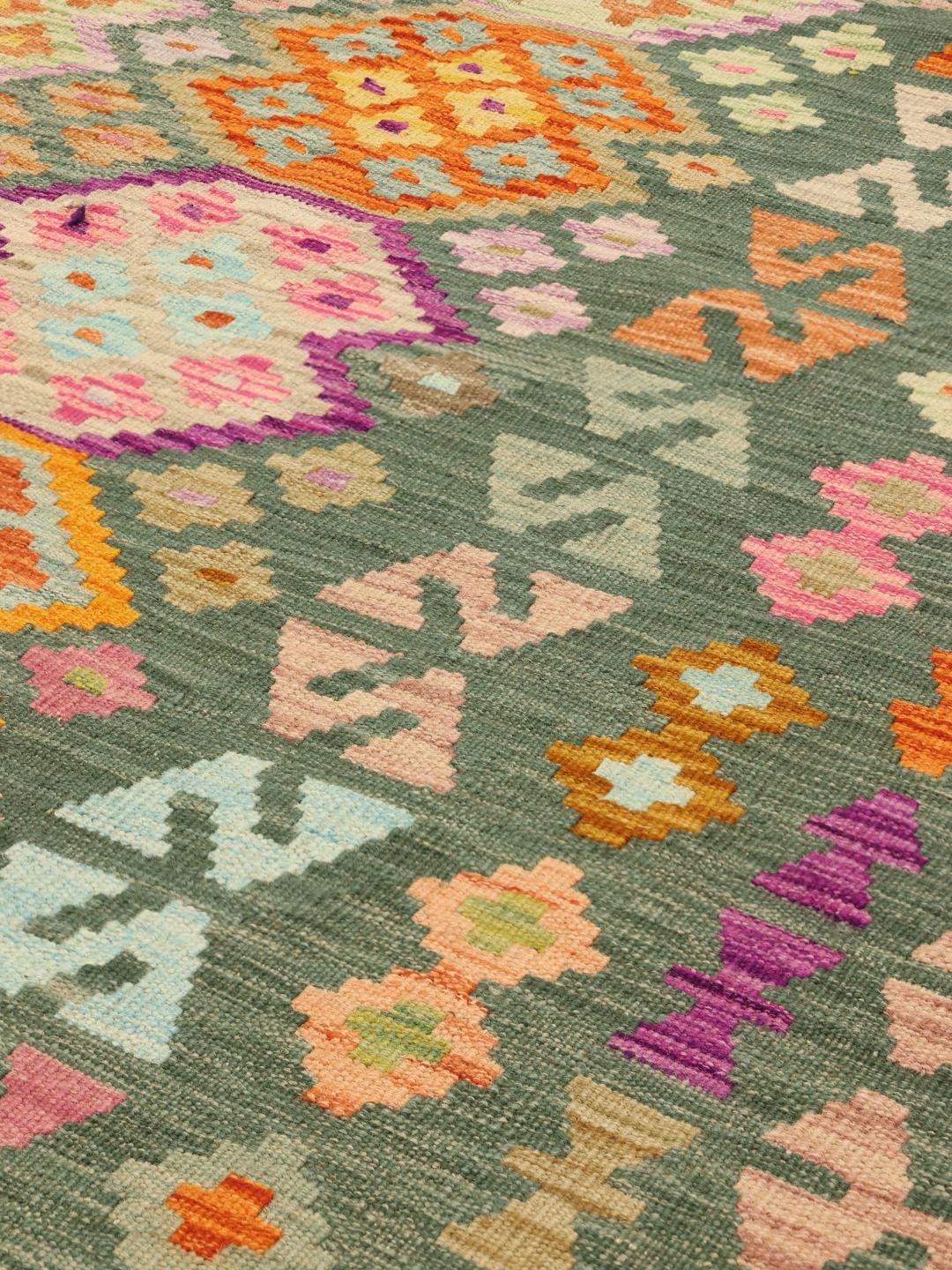 A large, rectangular Afghan Kelim rug featuring a multicolour geometric pattern on a green field.
