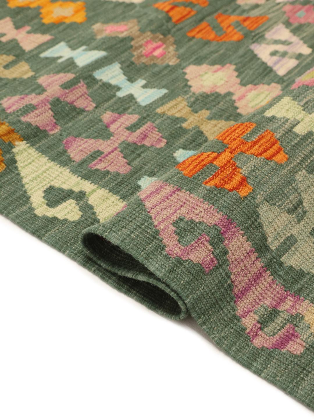A large, rectangular Afghan Kelim rug featuring a multicolour geometric pattern on a green field.