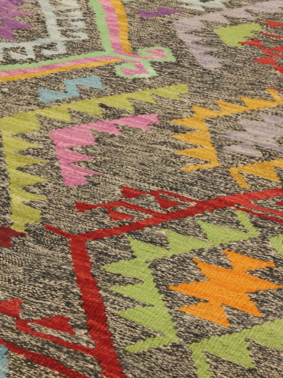 Hand-woven Afghan Kelim rug featuring a dark background with vibrant geometric patterns