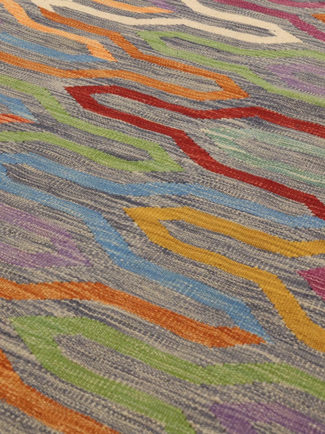 A vibrant, hand-woven Afghan kilim rug featuring a rhythmic, multicolored geometric pattern on a dark background.