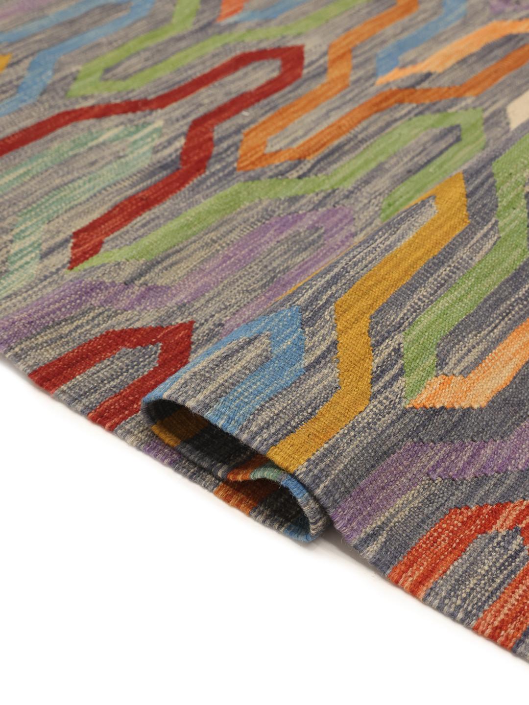A vibrant, hand-woven Afghan kilim rug featuring a rhythmic, multicolored geometric pattern on a dark background.