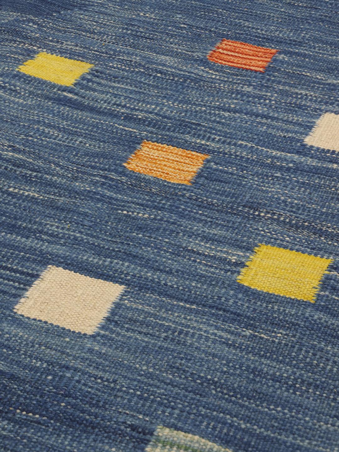 Een handgeweven Kilim-tapijt uit Afghanistan met een blauwe achtergrond en veelkleurige vierkante patronen.