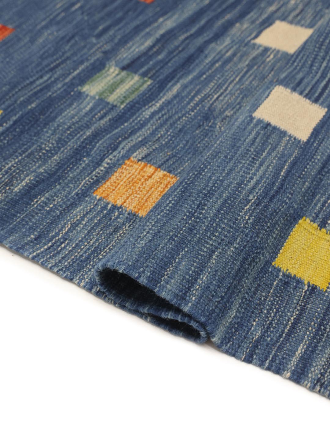 Een handgeweven Kilim-tapijt uit Afghanistan met een blauwe achtergrond en veelkleurige vierkante patronen.