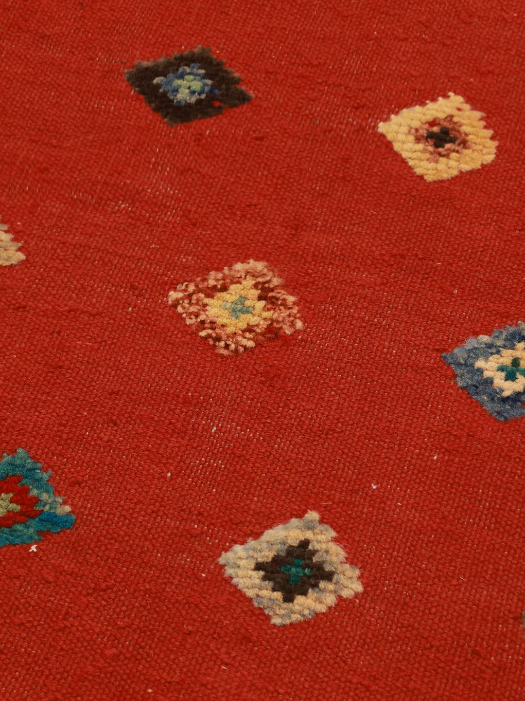 Um tapete retangular Kelim Nimbaft afegão com um campo vermelho vibrante e pequenos motivos geométricos de diamante multicoloridos.
