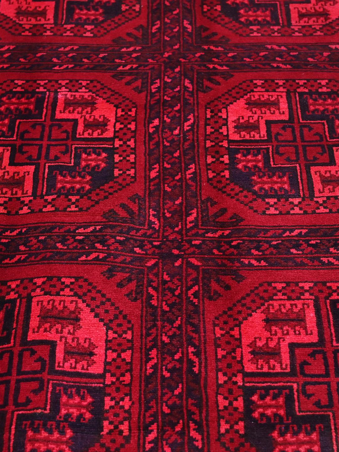 Tapis afghan Kunduz rouge noué à la main avec des motifs géométriques en médaillon.