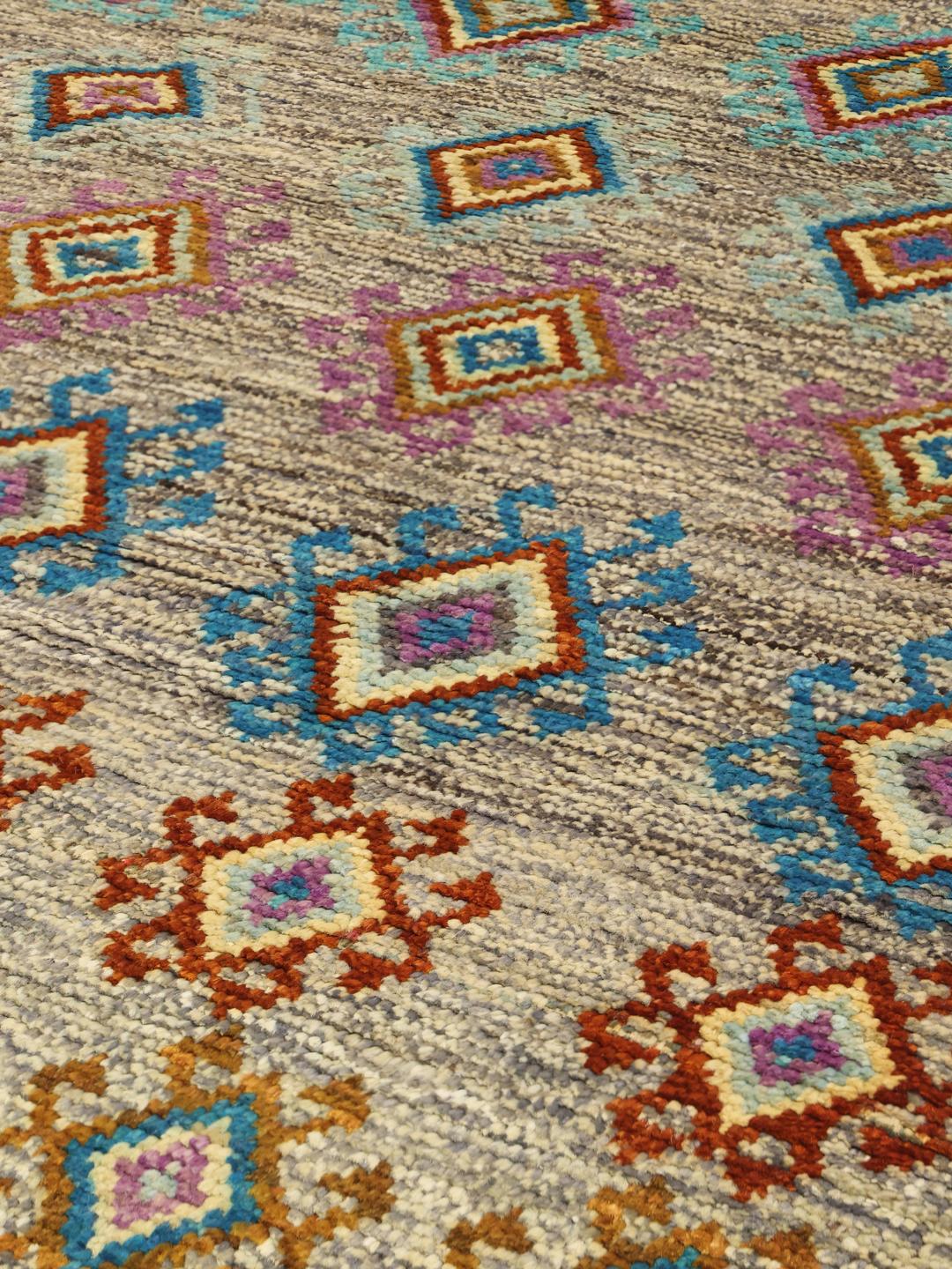 Hand-knotted Afghan rug with colourful geometric patterns on a grey background