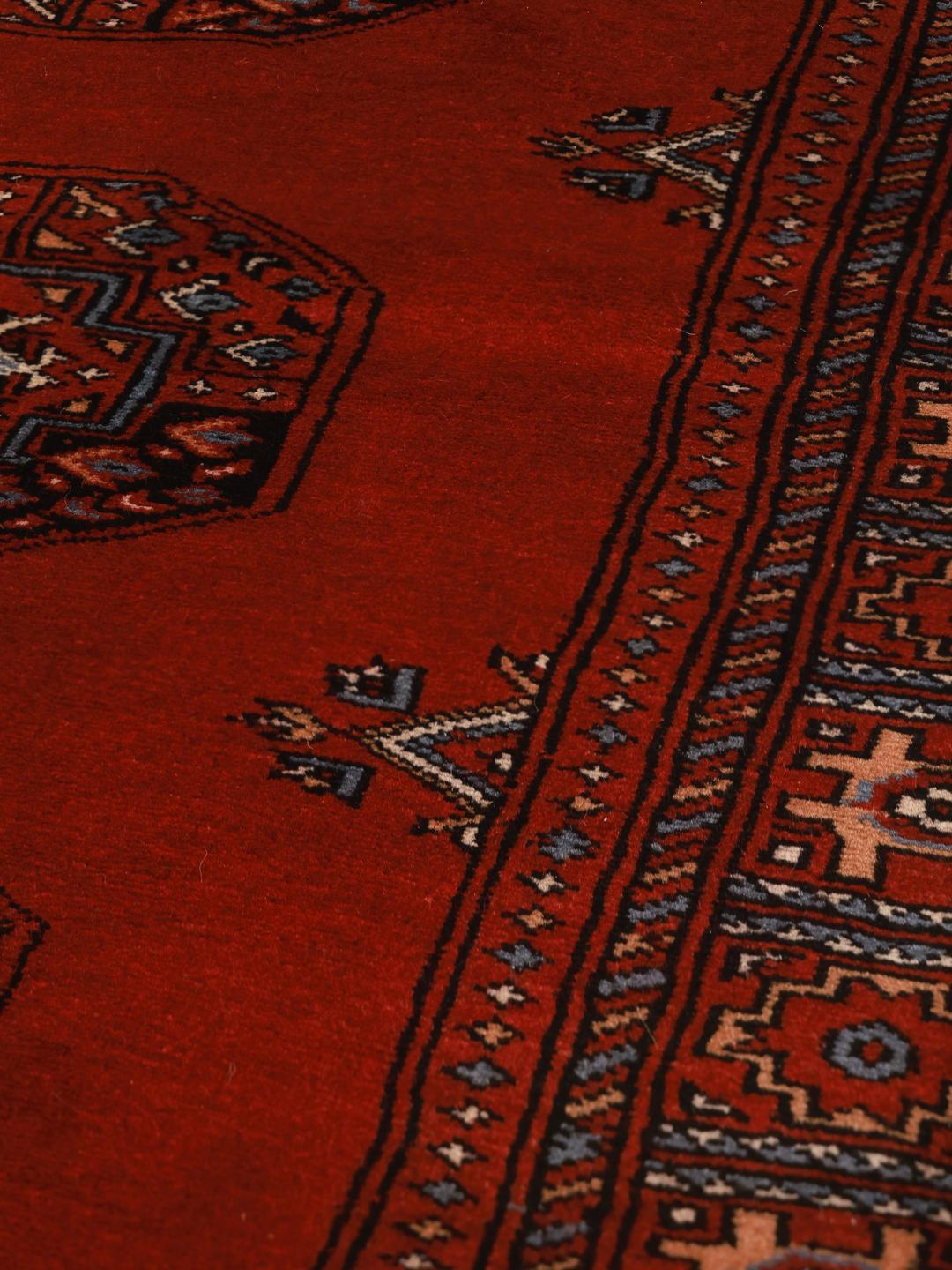 Red rug from Pakistan with traditional geometric motifs.