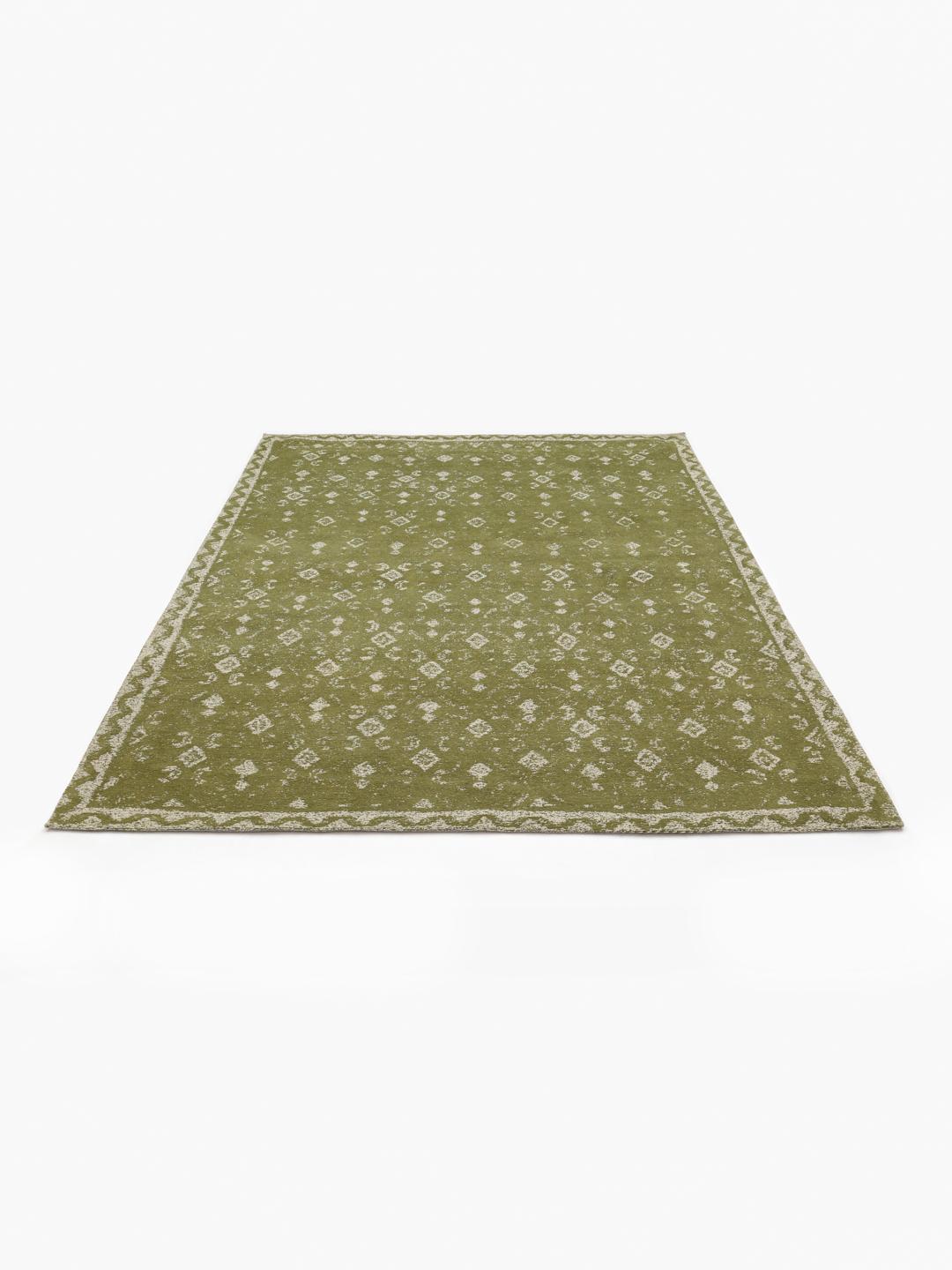 Handgeweven groen vloerkleed met een vervaagd geometrisch patroon en decoratieve rand