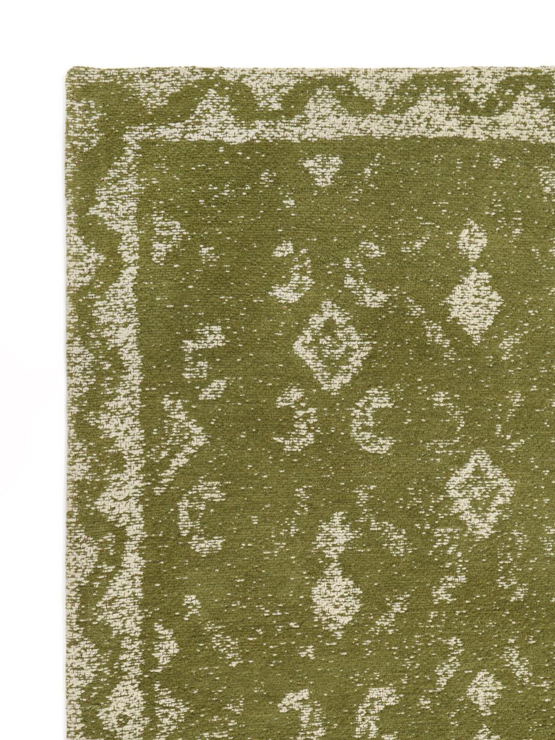 Handgeweven groen vloerkleed met een vervaagd geometrisch patroon en decoratieve rand