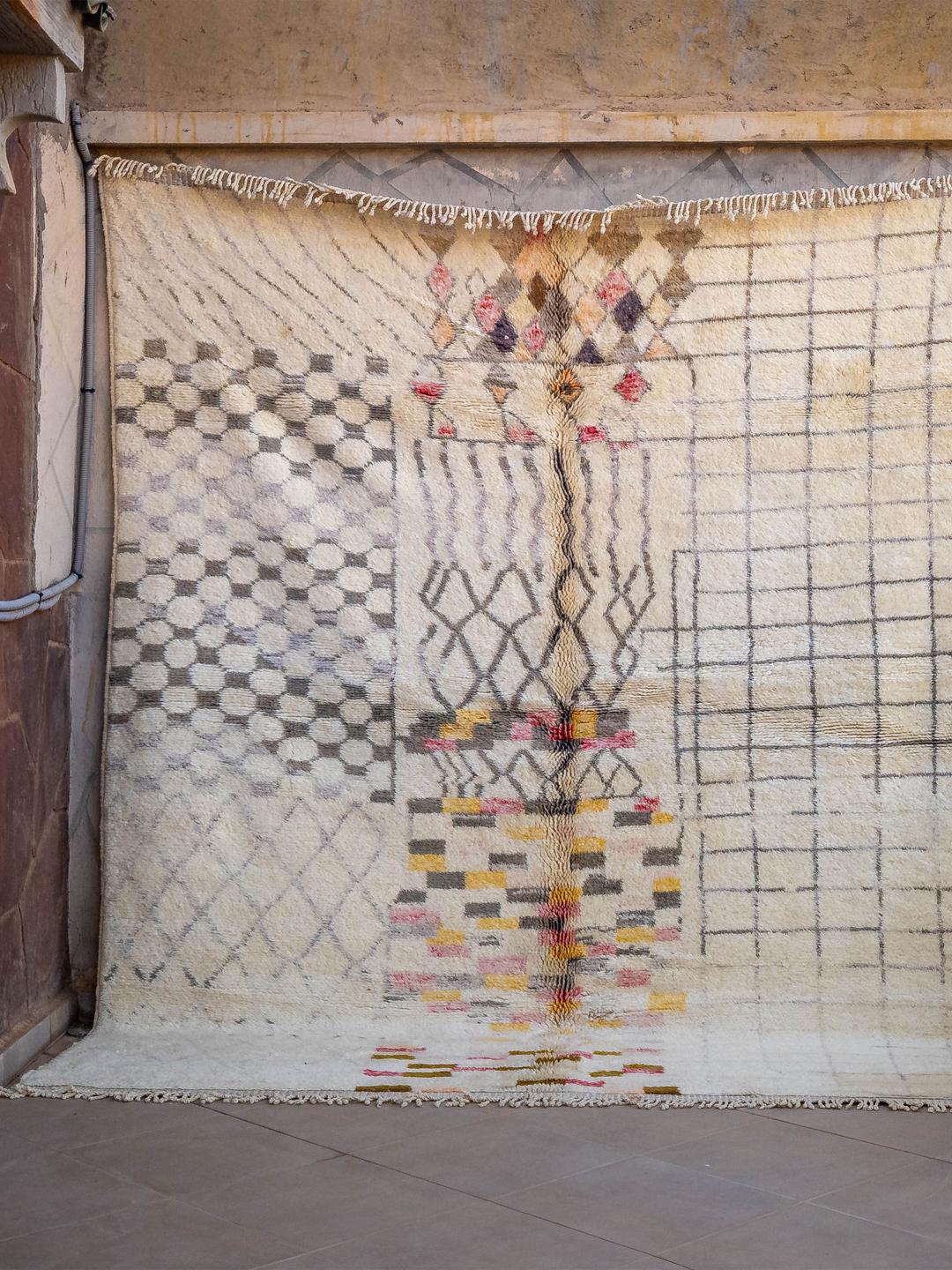 Un tapis marocain noué à la main avec un fond crème et des motifs géométriques multicolores.