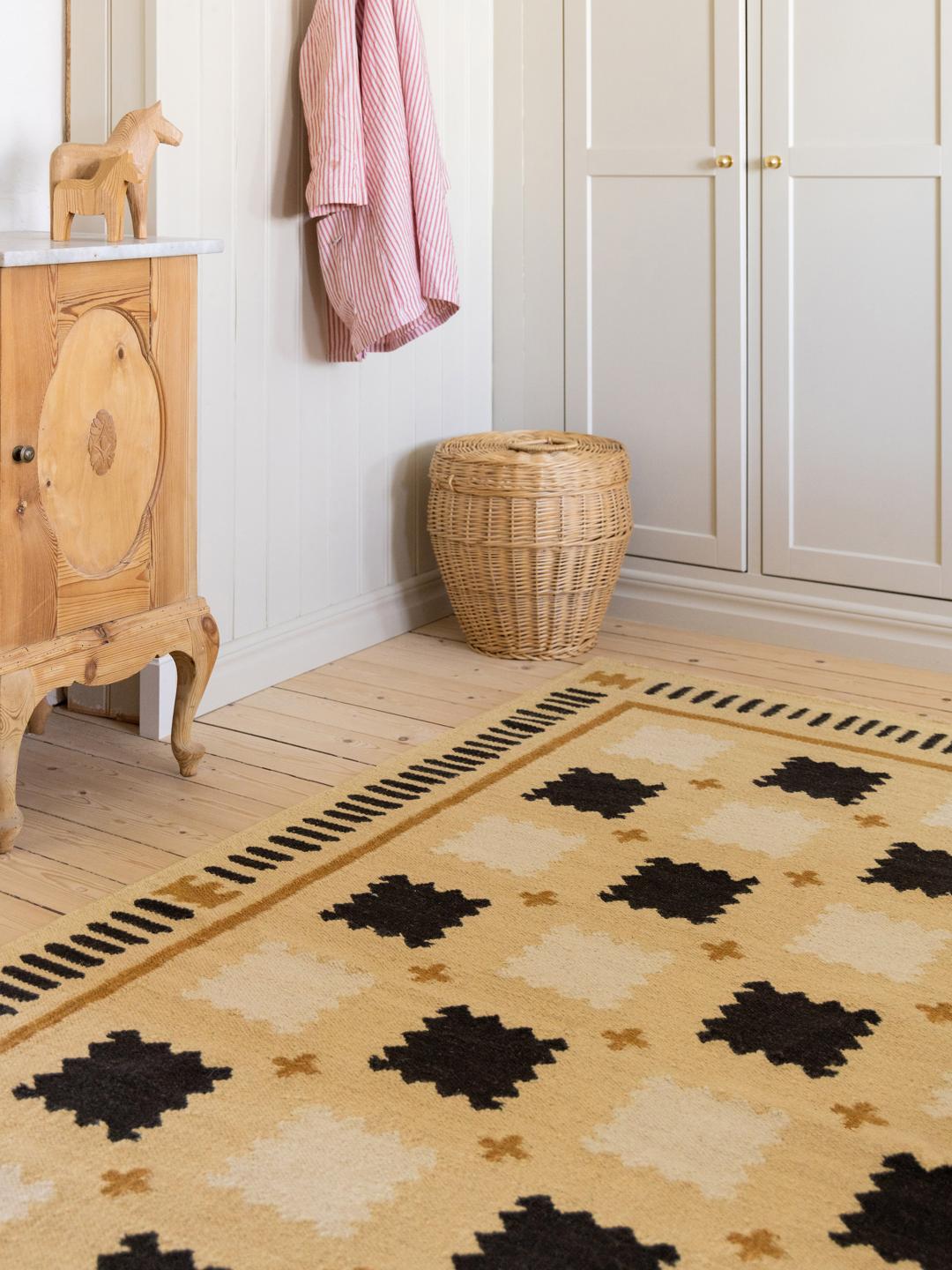 Een geel vloerkleed met een geometrisch patroon in zwarte en beige tinten.
