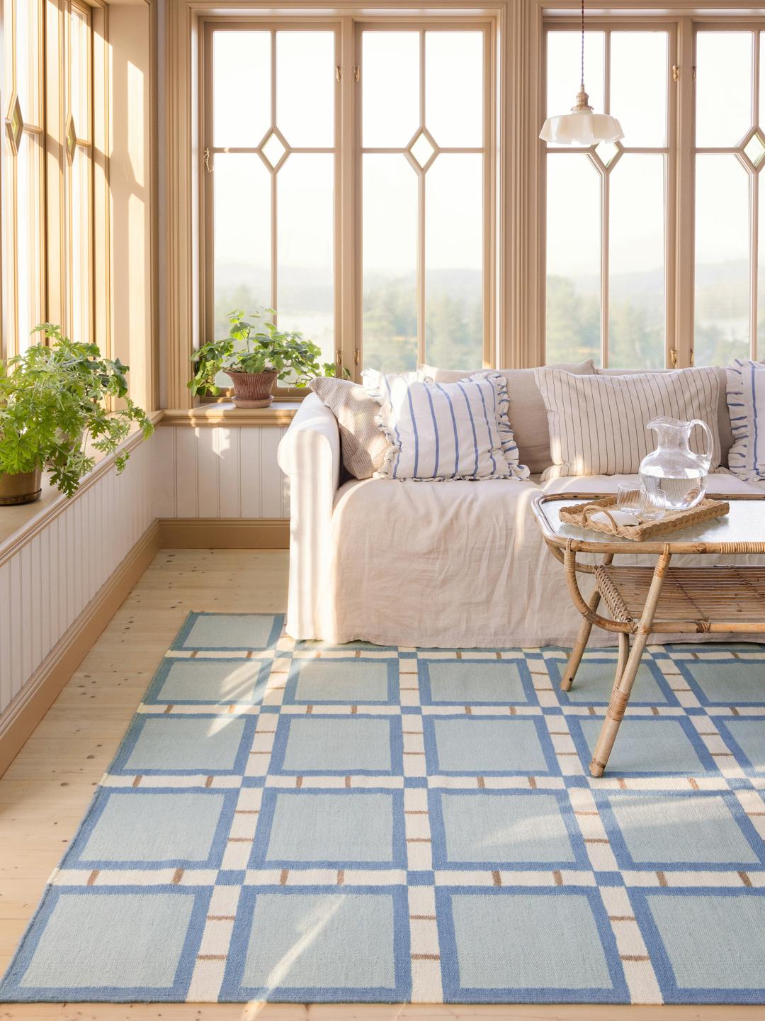 Een rechthoekig wollen vloerkleed met een geometrisch ruitpatroon in blauw, beige en wit.