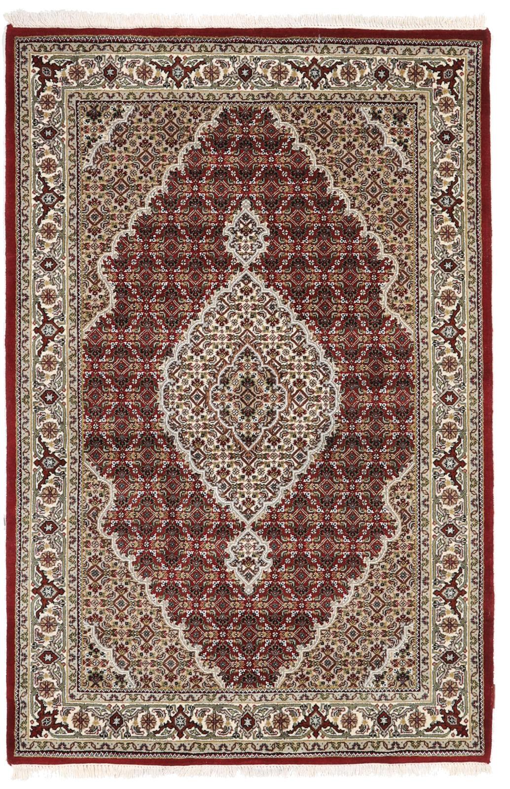 Een handgeknoopt Tabriz-tapijt uit India met een centraal medaillon op een rode ondergrond.