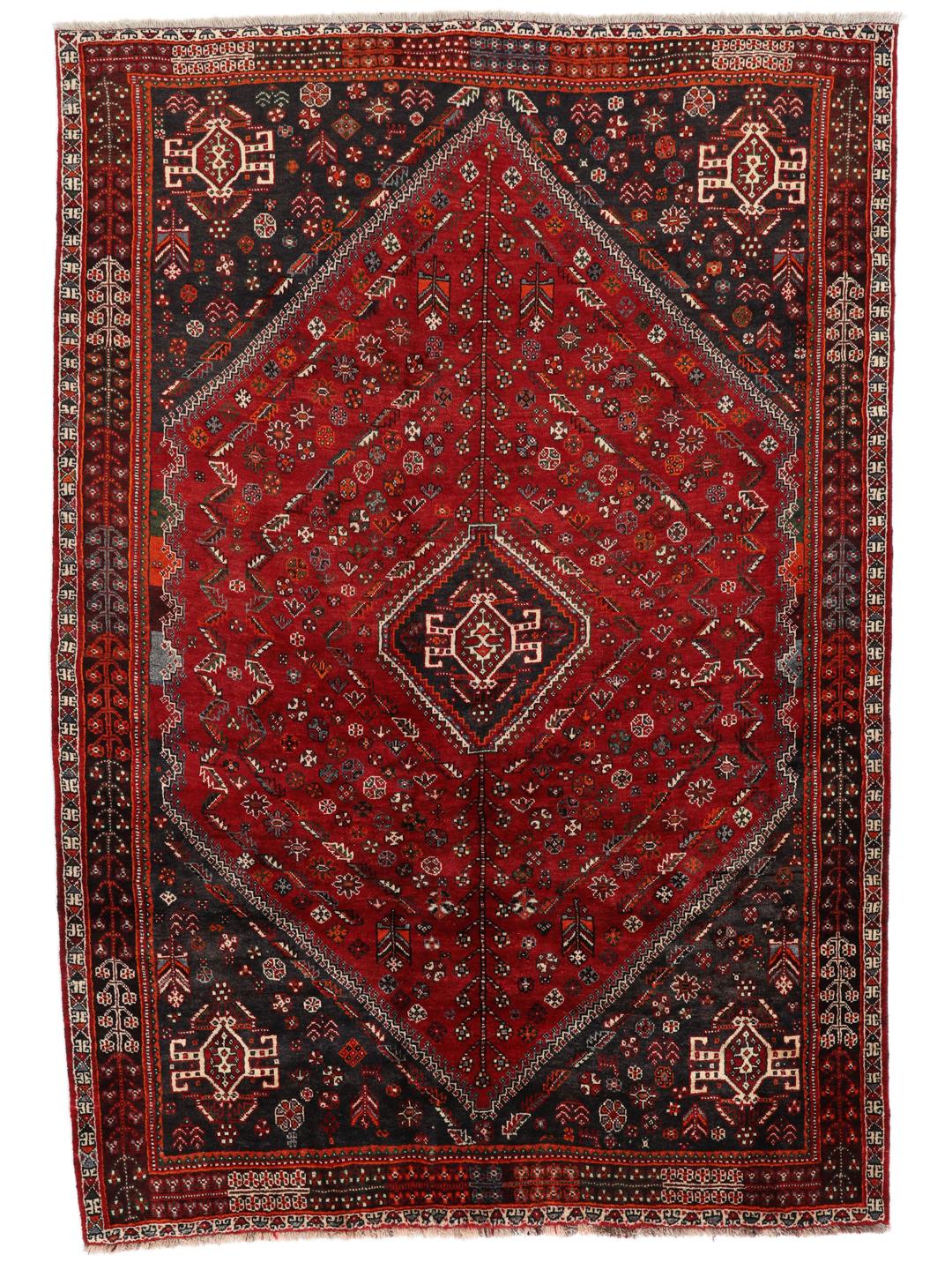 A hand-knotted Middle Eastern Ghashghai rug in red and dark tones with geometric patterns.