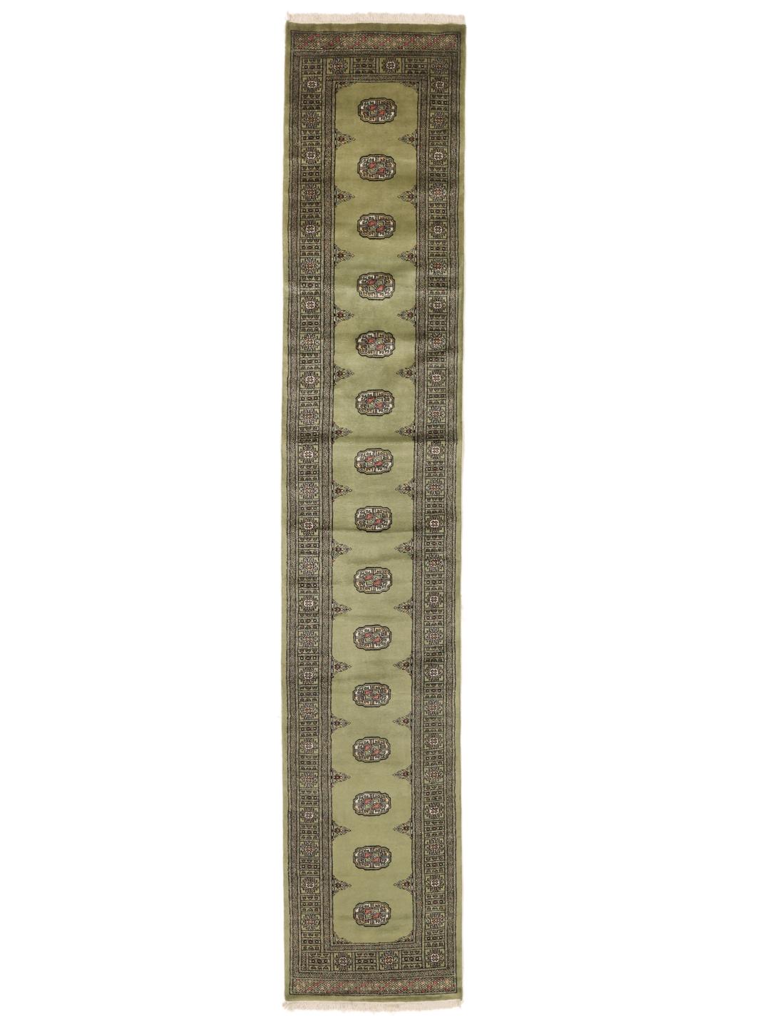 A long, narrow hand-knotted runner from Pakistan with a green field and traditional motifs.