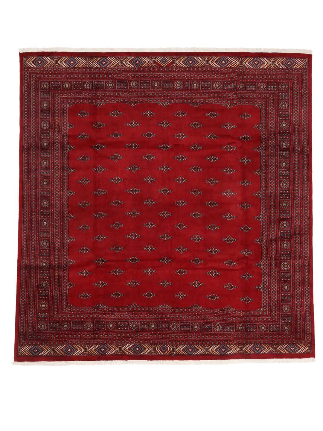 Een groot, vierkant Pakistan Bokhara vloerkleed met een dieprood veld en terugkerende geometrische motieven.