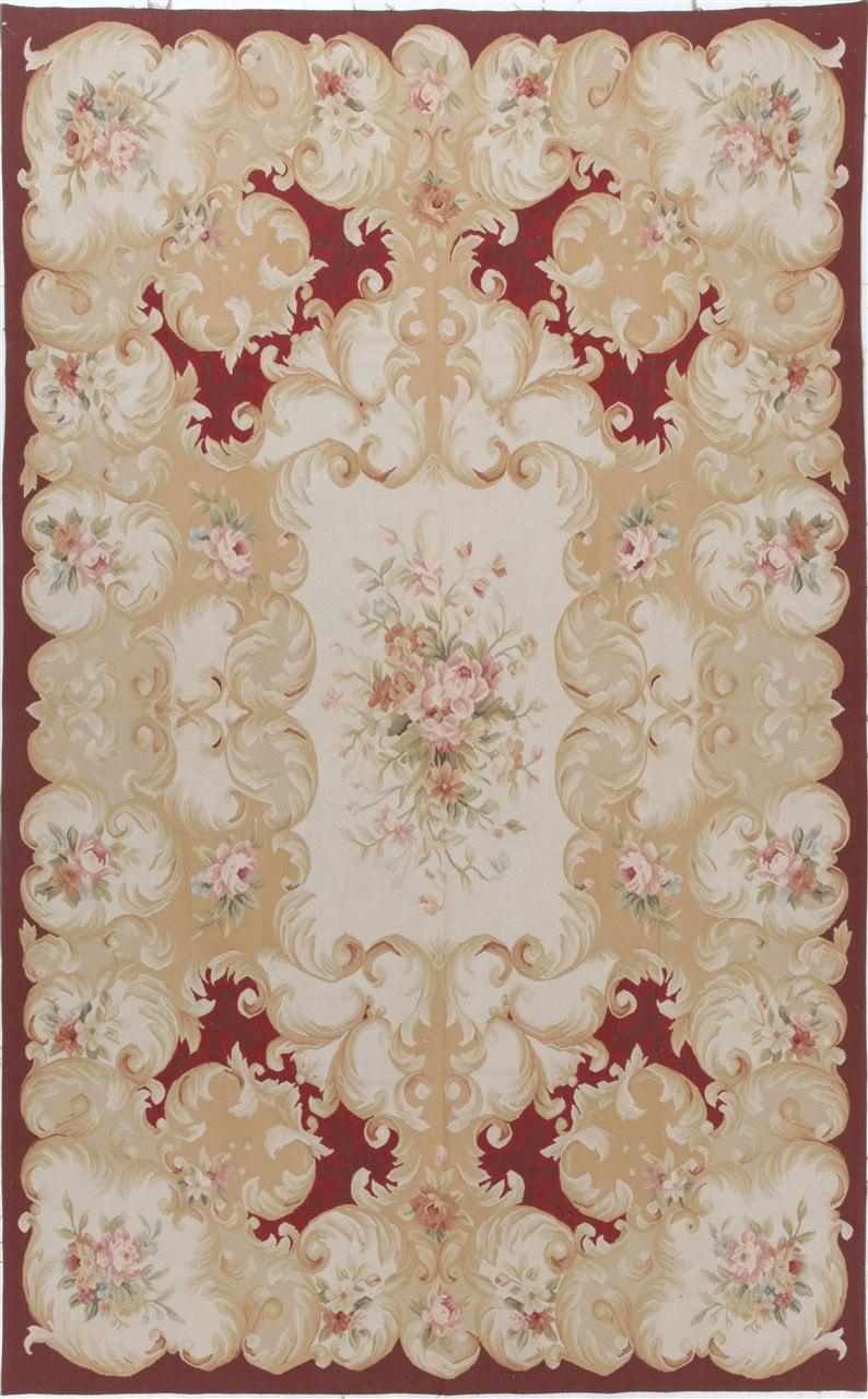Et rektangulært håndvævet Kilim-tæppe fra Kina med et blomstermønster i rødt og beige.