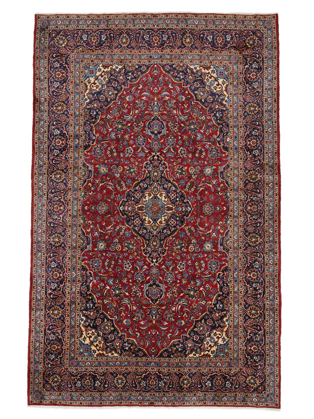 A large rectangular Keshan rug from the Middle East with a rich red floral field and blue accents.