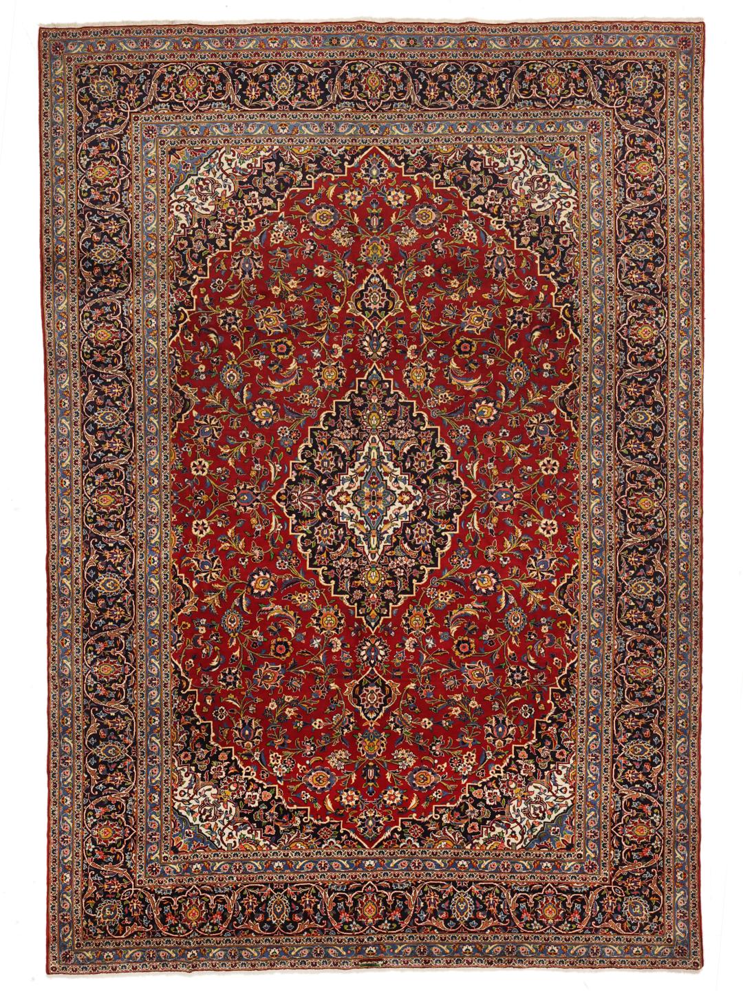 A large, hand-knotted Keshan rug from the Middle East with a deep red floral field and navy border.
