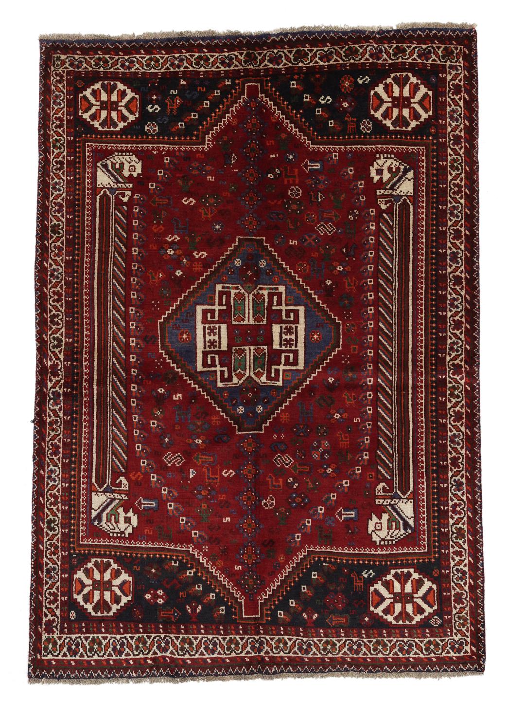 A red hand-knotted wool rug with geometric tribal patterns from the Middle East.