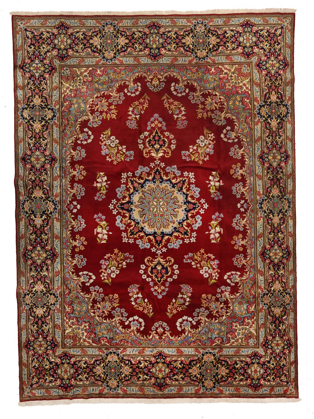 A large rectangular Kerman rug from the Middle East with a deep red field and intricate floral motifs.