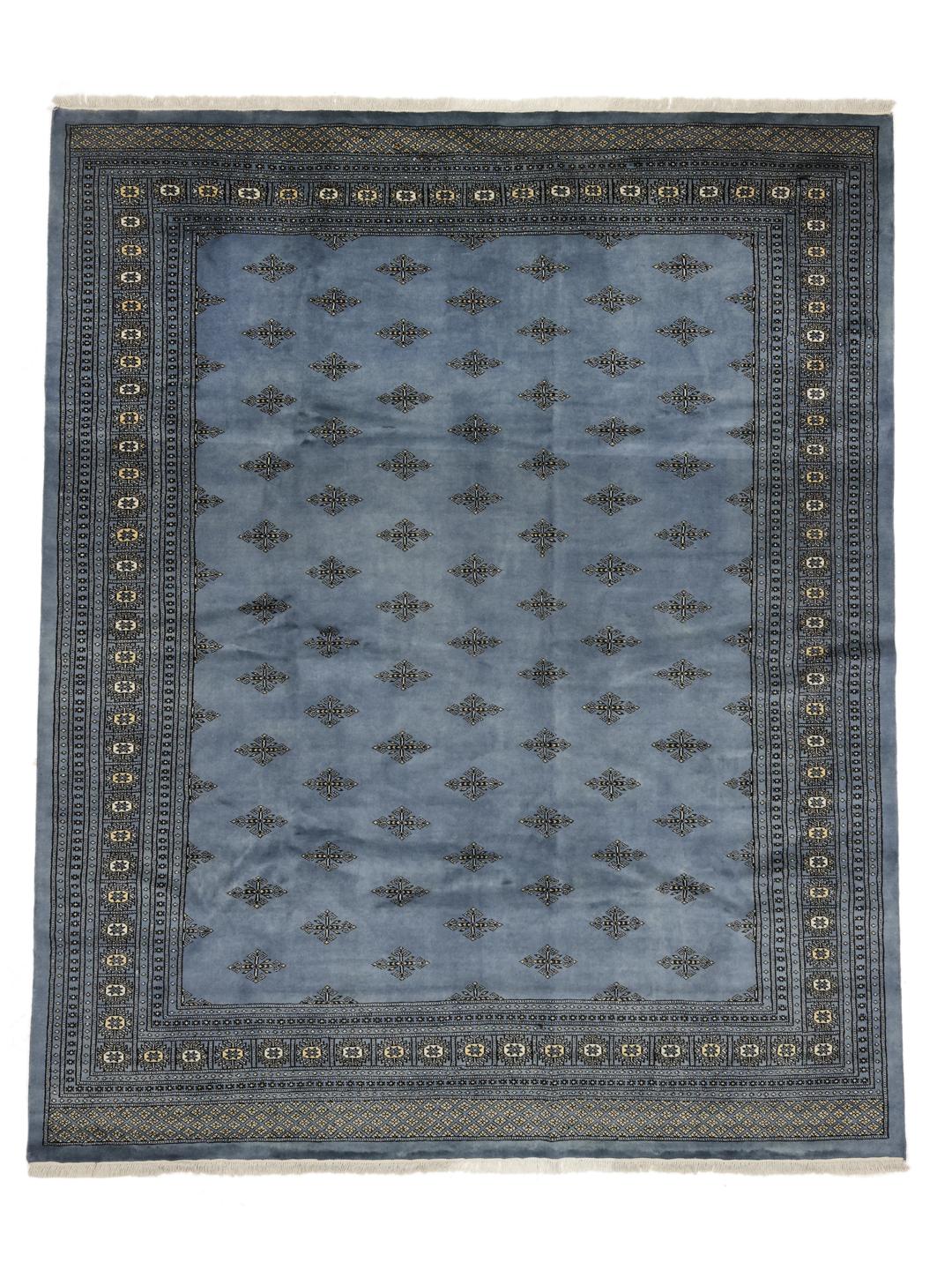 A hand knotted Bokhara rug from Pakistan in a soft blue color with intricate repeating motifs.